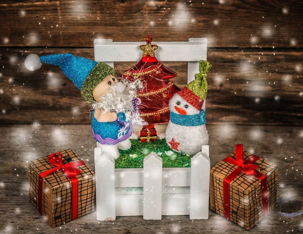 Santa y muñeco de nieve con dos cajas en el pueblo sobre fondo de madera  . — Foto de Stock