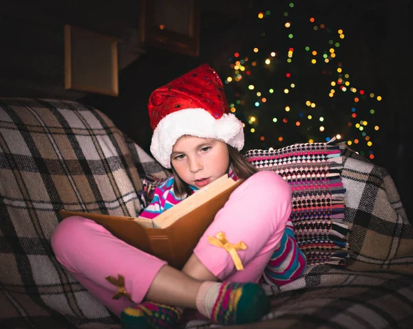 Überraschte junges Mädchen mit Weihnachtsmütze und Buch. — Stockfoto