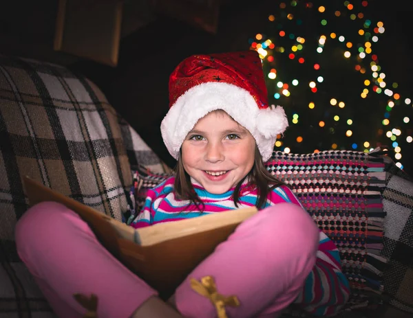 Überraschte junges Mädchen mit Weihnachtsmütze und Buch. — Stockfoto