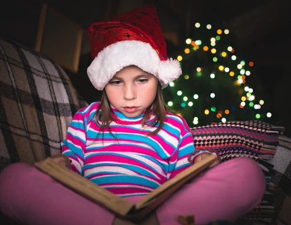 Überraschte junges Mädchen mit Weihnachtsmütze und Buch. — Stockfoto