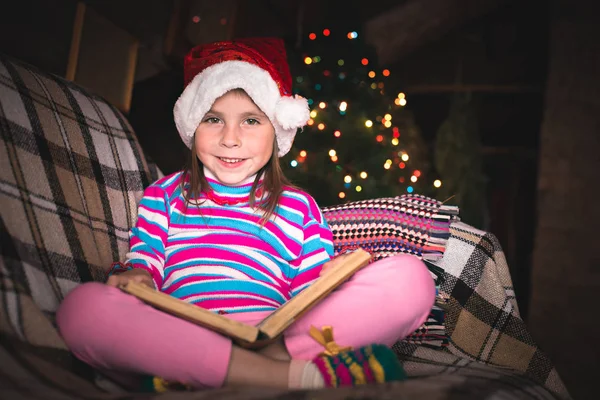 Überraschte junges Mädchen mit Weihnachtsmütze und Buch. — Stockfoto