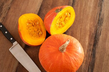 Küçük ve yarı rengarenk portakal renginde bir balkabağı ya da mutfak masasında büyük bir bıçakla kabak, yüksek açılı bir manzara.