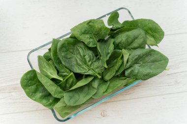 Işık arka planında şeffaf bir kasede ıspanak. Sağlıklı yeme kavramı.