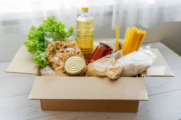 Mallarla dolu bağış kutusu, komşulara karantina yardımı konsepti. Yağ, konserve yiyecek, makarna, domates ezmesi, elma.