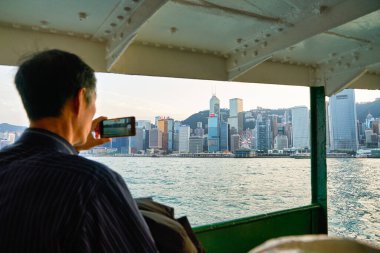 HONG KONG, CHINA - CIRCA JANUARY, 2019: man on a Star Ferry taking photo of Hong Kong. (Focus on skyline)