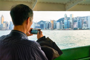 HONG KONG, CHINA - CIRCA JANUARY, 2019: man on a Star Ferry taking photo of Hong Kong. (Focus on smartphone)