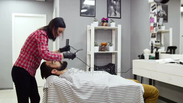 Barbeiro mulher aparando barba de cliente com clipper na barbearia . — Vídeo de Stock