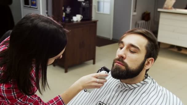 Barbier femme taille barbe du client avec tondeuse au salon de coiffure . — Video