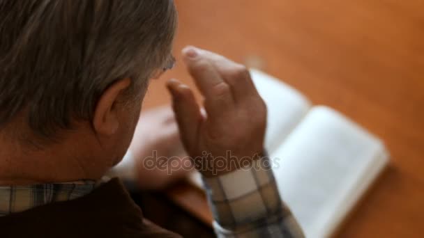 Viejo sentado en el sofá en casa leyendo un libro — Vídeos de Stock