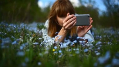 Genç bir kız çiçeklerin fotoğraflarını akıllı telefondan çekiyor.