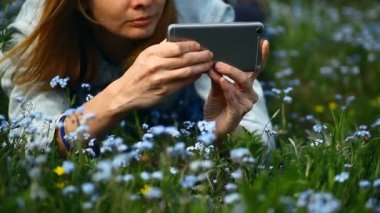 Genç bir kız çiçeklerin fotoğraflarını akıllı telefondan çekiyor.