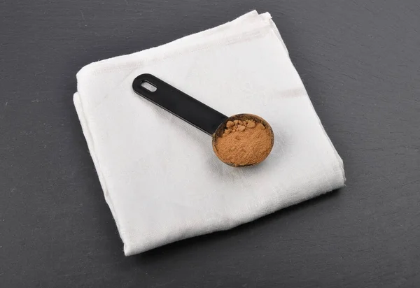 Polvo de algarroba en cuchara dosificadora sobre pizarra —  Fotos de Stock