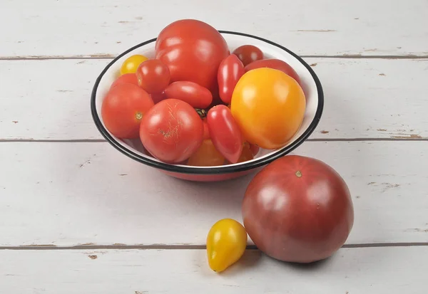 Verscheidenheid van tomaat cultivars in emaille kom op verweerd hout — Stockfoto