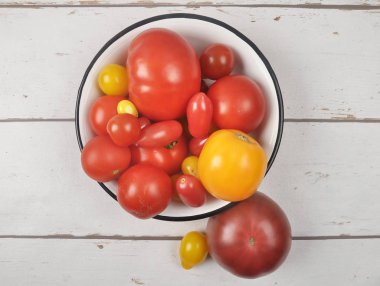 Domates çeşitlerin emaye kase yıpranmış ahşap üzerine çeşitli