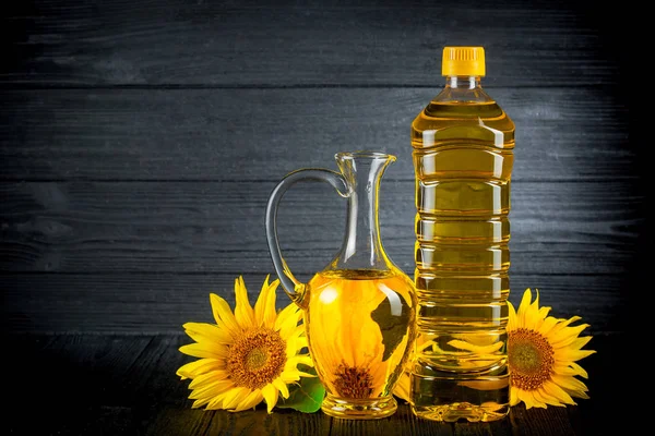 Aceite de girasol con flores sobre fondo rústico negro — Foto de Stock