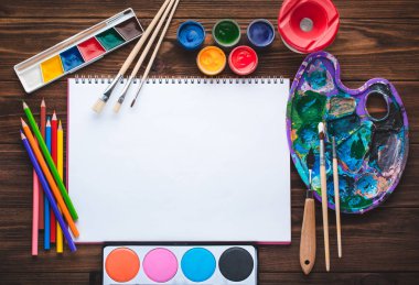 Boyalar, kalemler, sketchbook vintage ahşap zemin üzerine resim ve boş beyaz kağıt yaprağının için araçlar kümesi. Üstten görünüm.