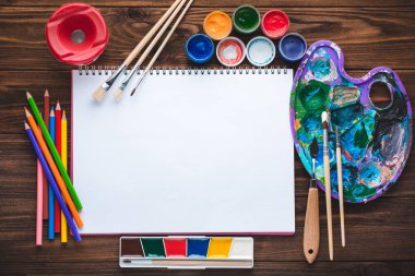 Boyalar, kalemler, sketchbook vintage ahşap zemin üzerine resim ve boş beyaz kağıt yaprağının için araçlar kümesi. Üstten görünüm.