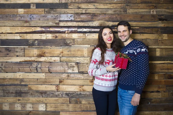 Young couple near wooden wall celebrating Christmas — Stock Photo, Image