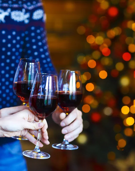 Tintinnante bicchieri di vino rosso in mano su luci di Natale backgr — Foto Stock