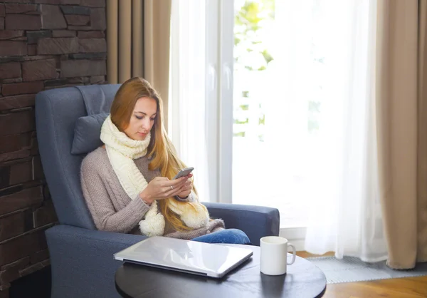 Woman in armchair writing a text message on her cell phone — Stock Photo, Image