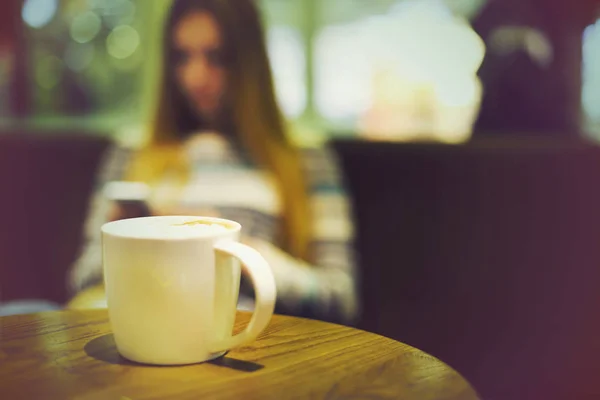Кофейная чашка в кафе и женщина с мобильным телефоном — стоковое фото