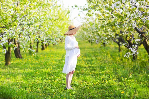 Mulher grávida vestindo chapéu grande e vestido branco em garde florescendo — Fotografia de Stock