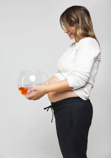 Happy pregnant woman holding a fishbowl with a goldfish in her h — Stock Photo, Image