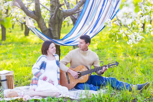 Pregnant couple in blooming garden at the picnic — Stock Photo, Image