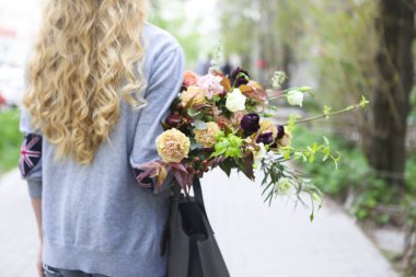 Çanta ve buket ile sokakta yürüyen genç güzel kadın