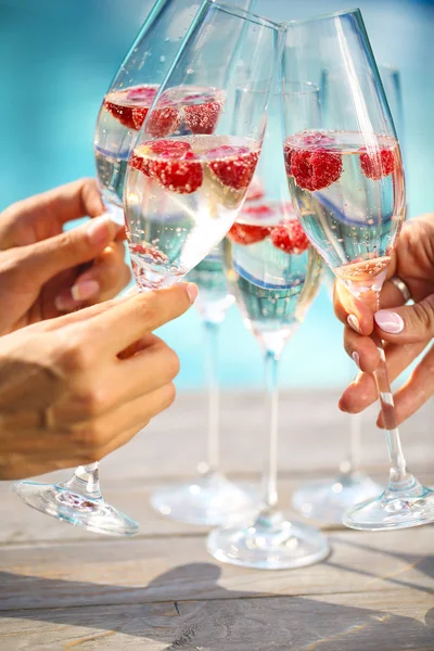 Mãos com taças de champanhe com framboesa — Fotografia de Stock