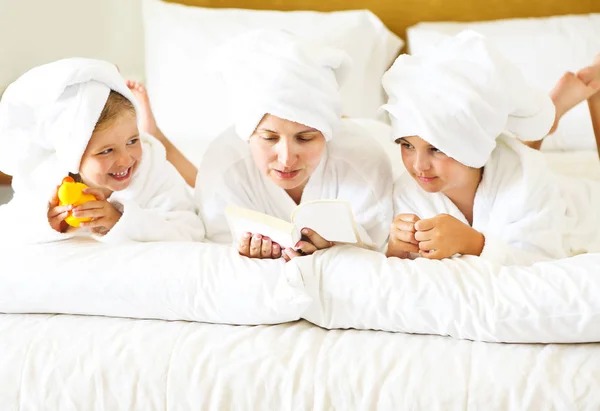 Gelukkig moeder en meisjes in badjassen in de slaapkamer. Mantelzorg en — Stockfoto
