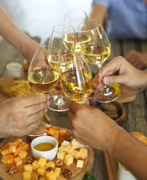 Mãos com vinho branco torrando sobre mesa servida com comida — Fotografia de Stock