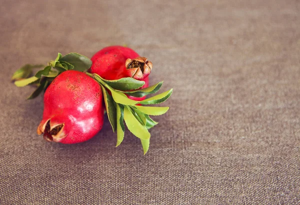 Két gránátalma gyümölcs, levelek, textil háttér — Stock Fotó