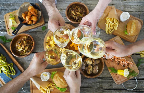 People with white wine toasting over served table with food.