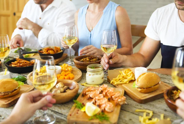 Persone con vino bianco che brindano sulla tavola servita con cibo . — Foto Stock