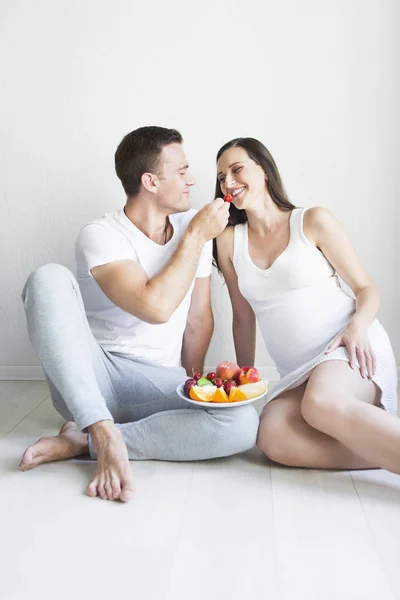 Young man and pregnant woman with fruit plate indoors — Stock Photo, Image