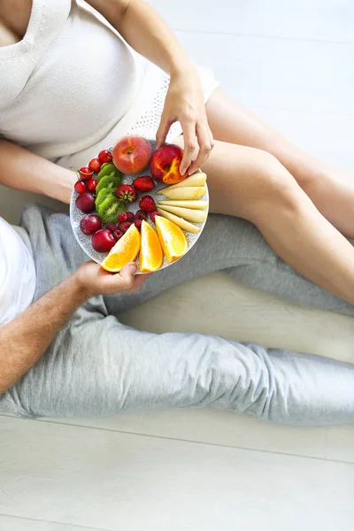 Jovem e mulher grávida sentados com prato de frutas — Fotografia de Stock