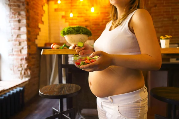 Mujer embarazada joven comiendo ensalada de verduras frescas en la cocina —  Fotos de Stock