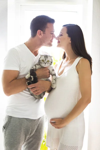 Young man with pregnant woman and cat indoors — Stock Photo, Image