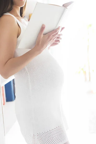 Ung vacker gravid kvinna läser bok inomhus — Stockfoto
