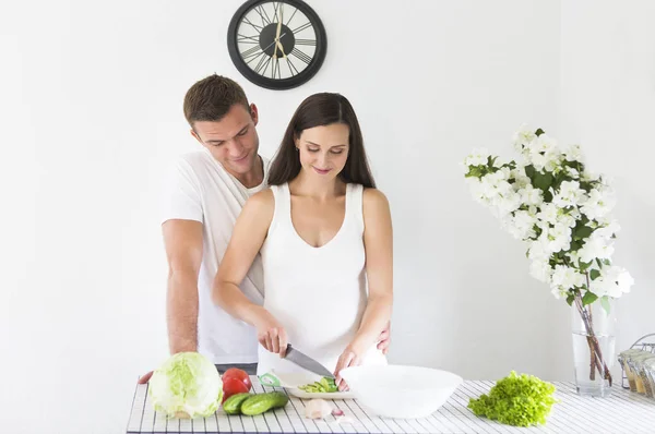 Hombre joven y bonita mujer embarazada cocinando en la cocina —  Fotos de Stock