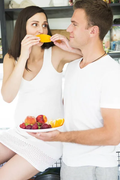 Jonge man en zwangere vrouw met vruchten plaat binnenshuis — Stockfoto