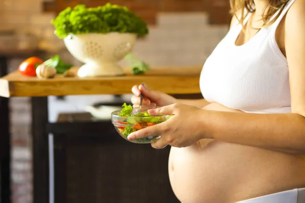 Jovem grávida comendo salada de legumes frescos na cozinha — Fotografia de Stock