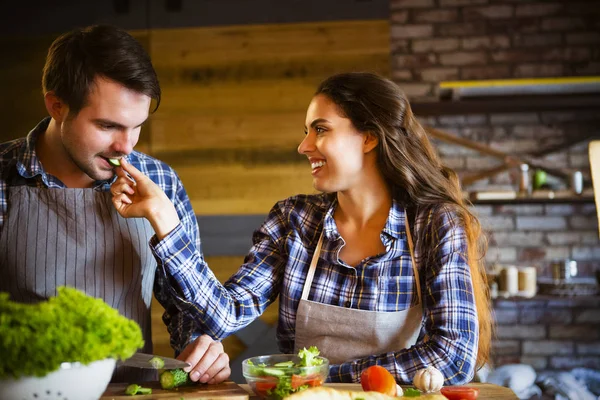 Young man and woman cooking and eating together at kitchen — Stock Photo, Image