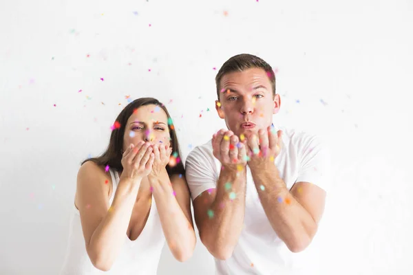 Young man and woman blowing confetti decorations — Stock Photo, Image