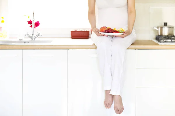 Красивая молодая беременная женщина с фруктами на кухне — стоковое фото
