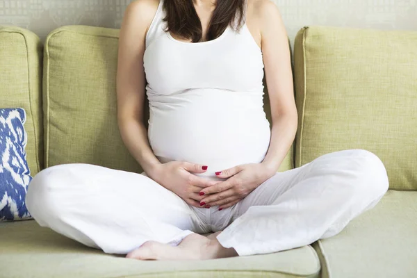 Молодая красивая беременная женщина сидит на диване — стоковое фото