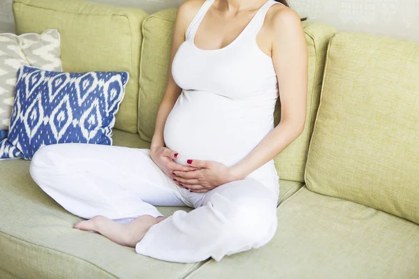 Mladá docela těhotná žena sedí na pohovce — Stock fotografie
