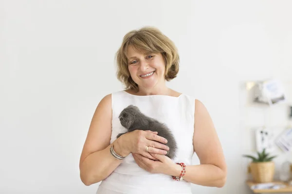 Pequeno gato cinza sentado em mãos de mulher madura — Fotografia de Stock