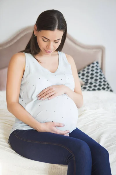 Беременная женщина в помещении сидит на кровати — стоковое фото